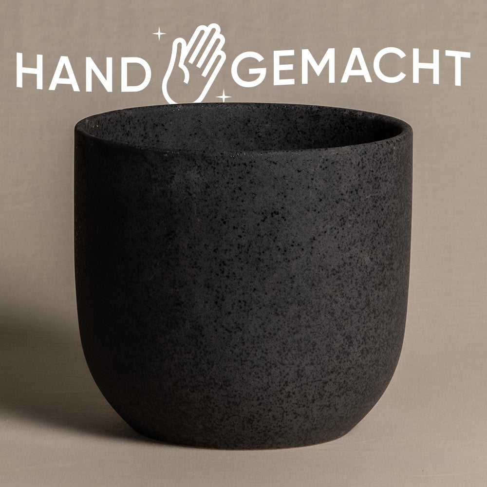 Ein strukturierter, dunkelfarbiger, heller Keramik-Topf (Direito | 18 cm ⌀) ist zentriert vor einem neutralen Hintergrund platziert. Darüber ist das Wort „HANDGEMACHT“ in fetten weißen Buchstaben zu sehen, mit einer stilisierten Handgrafik zwischen den Wörtern.