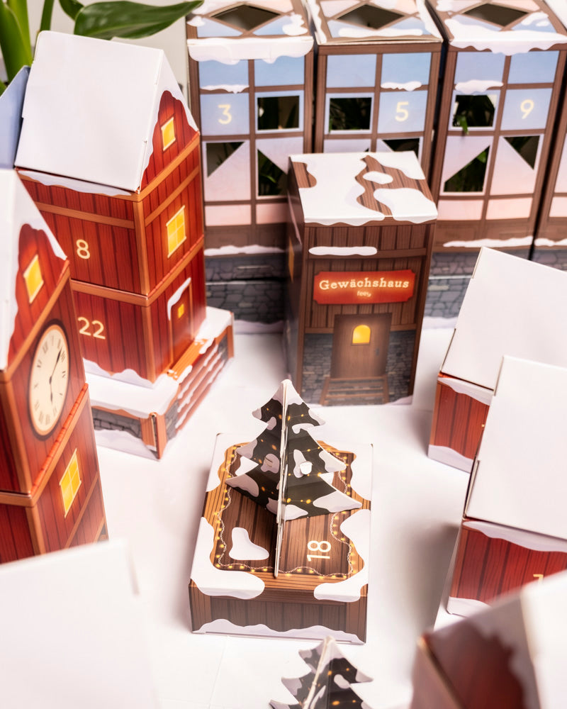 Eine festliche Szene mit roten und braunen schneebedeckten Gebäuden, die wie der Pflanzen-Adventskalender nummeriert sind, mit einem Mini-Weihnachtsbaum in der Mitte, einem 